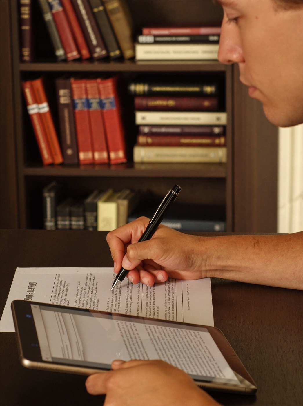 Mão assinando um contrato com caneta-tinteiro, estante de livros jurídicos ao fundo