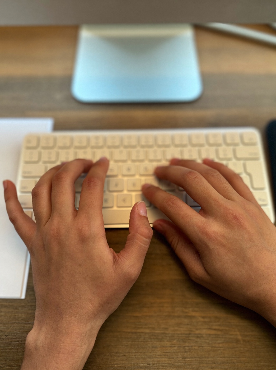 Mãos digitando em um teclado branco avulso sobre uma mesa de madeira